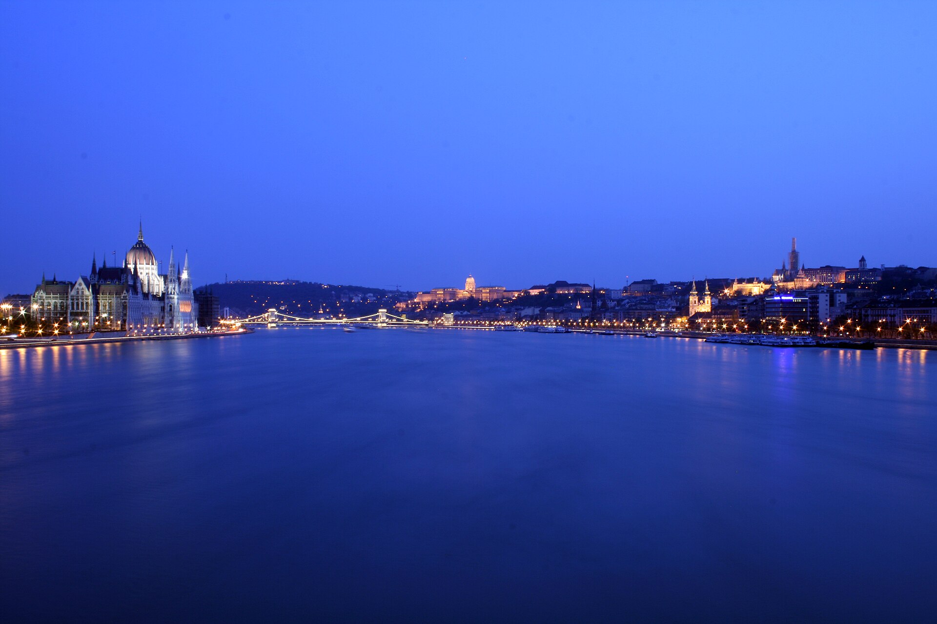 Panorámica nocturna del Danubio en Budapest con el Parlamento iluminado a la izquierda y el Castillo de Buda al fondo.