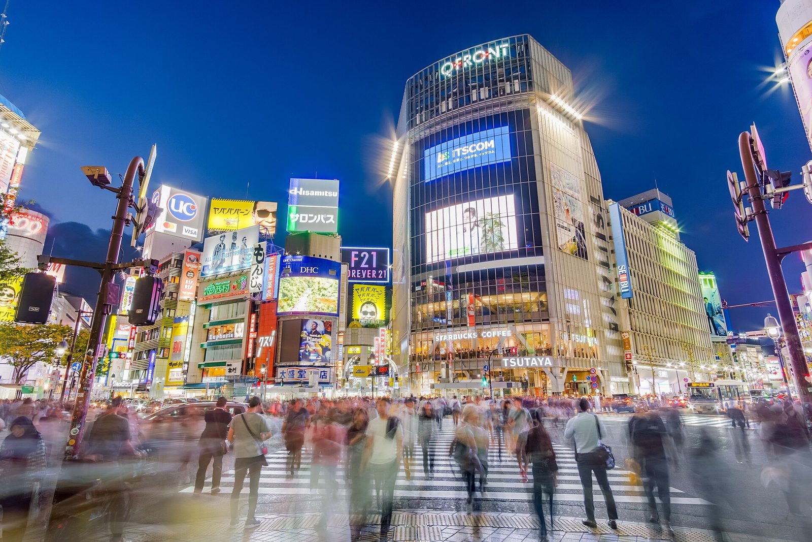 Cruce de Shibuya de noche con pantallas iluminadas y peatones en movimiento.