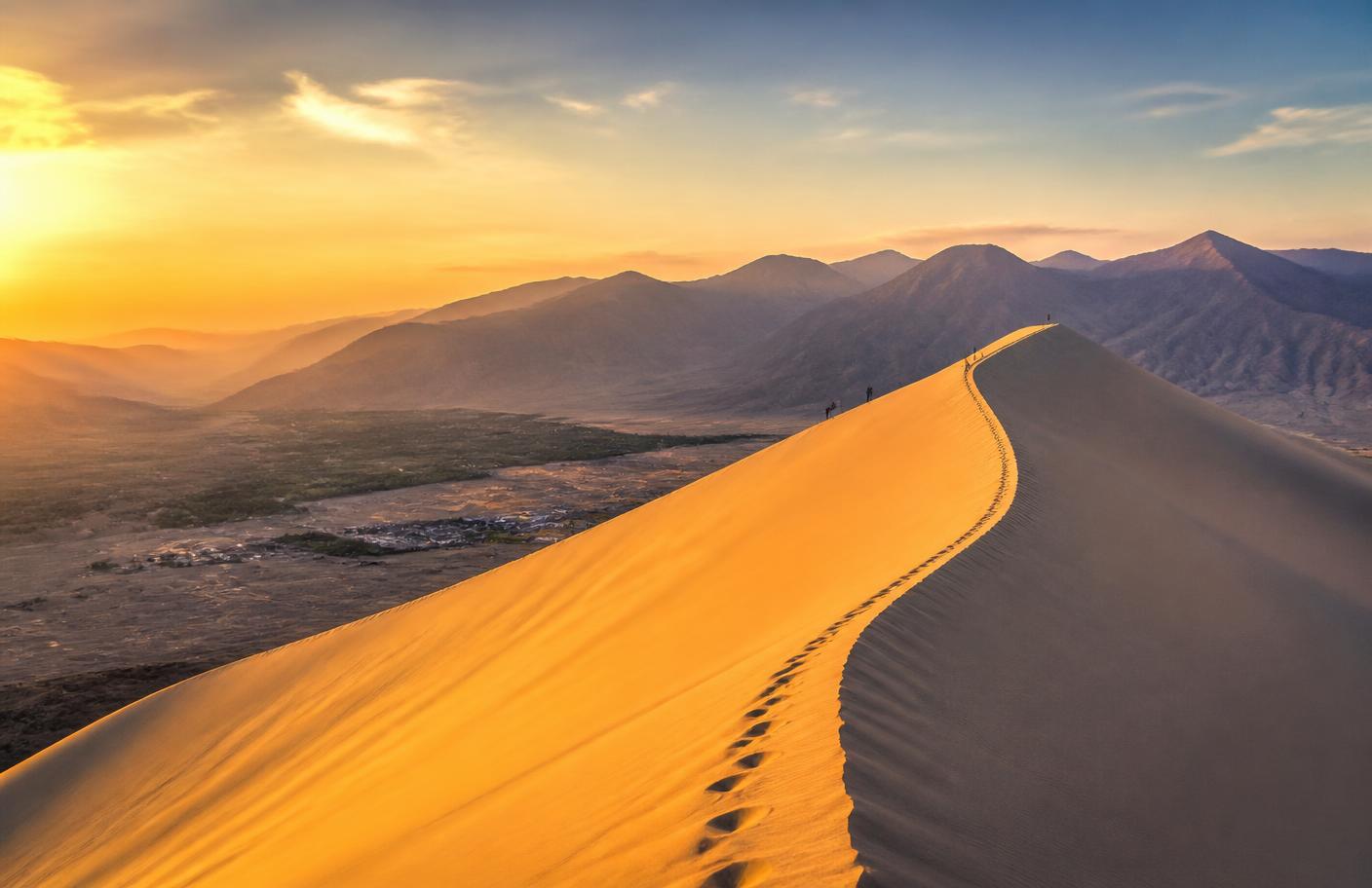 Gran duna de arena dorada al amanecer sobre un valle desértico del Perú