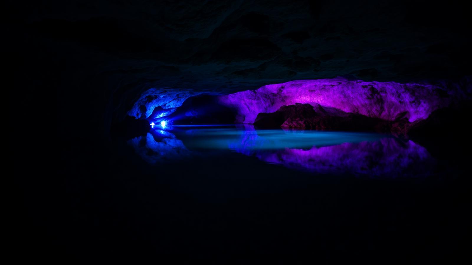 Lago subterráneo de aguas quietas iluminado con luces azules y violetas dentro de una mina