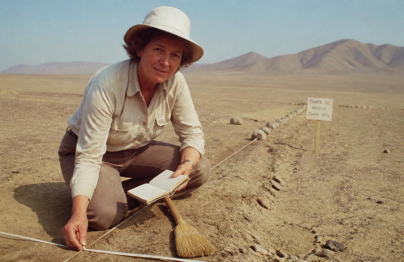 Investigadora midiendo líneas en el desierto de Nazca con cinta métrica y cuaderno